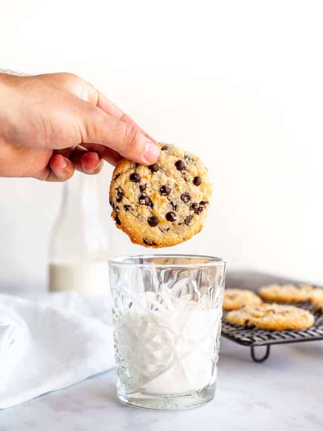 hand holding a chocolate chip cookie over a glass of milk