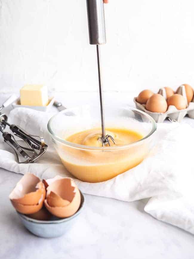 whisk inside mixing bowl on white table with eggs